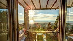 Un balcon agrémenté de fauteuils et d’une table en osier, offrant une vue panoramique sur la mer et les montagnes.