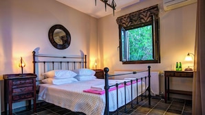 Un lit bien fait, avec une couette et des oreillers blancs, une table de chevet avec une lampe, une fenêtre donnant sur un paysage verdoyant et un radiateur placé sous la fenêtre.