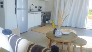 Eine moderne Küche mit weißen Schränken, einem integrierten Backofen und einer Waschmaschine. Ein runder Holztisch mit einer Vase gefüllt mit Trockenpflanzen und einer Schüssel.