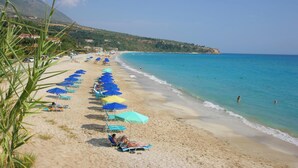 Ein Strand mit blauen und gelben Sonnenschirmen, einem Sandstrand und einem klaren, blauen Meer.