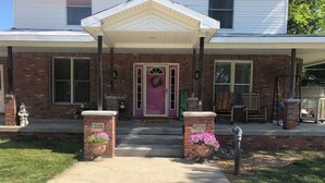A brick house with a front porch, a pink door, and two flower planters.