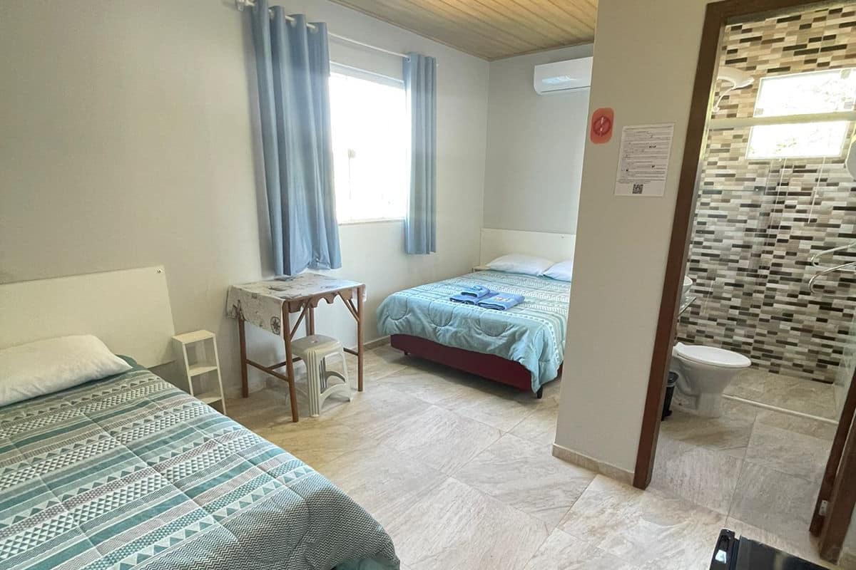 A room with two beds, a desk, a chair, a small table, a television, and a bathroom visible through an open door.