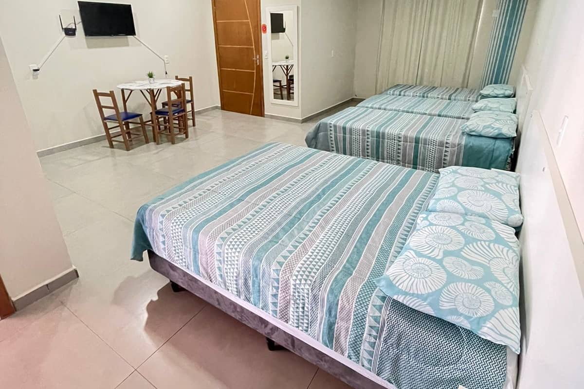 A hotel room with two beds, a desk with a chair, a TV mounted on the wall, and a door with a small window.