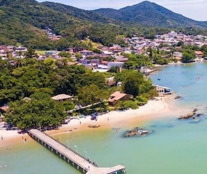 Vue aérienne d’une ville côtière avec une plage, une jetée et une végétation luxuriante.