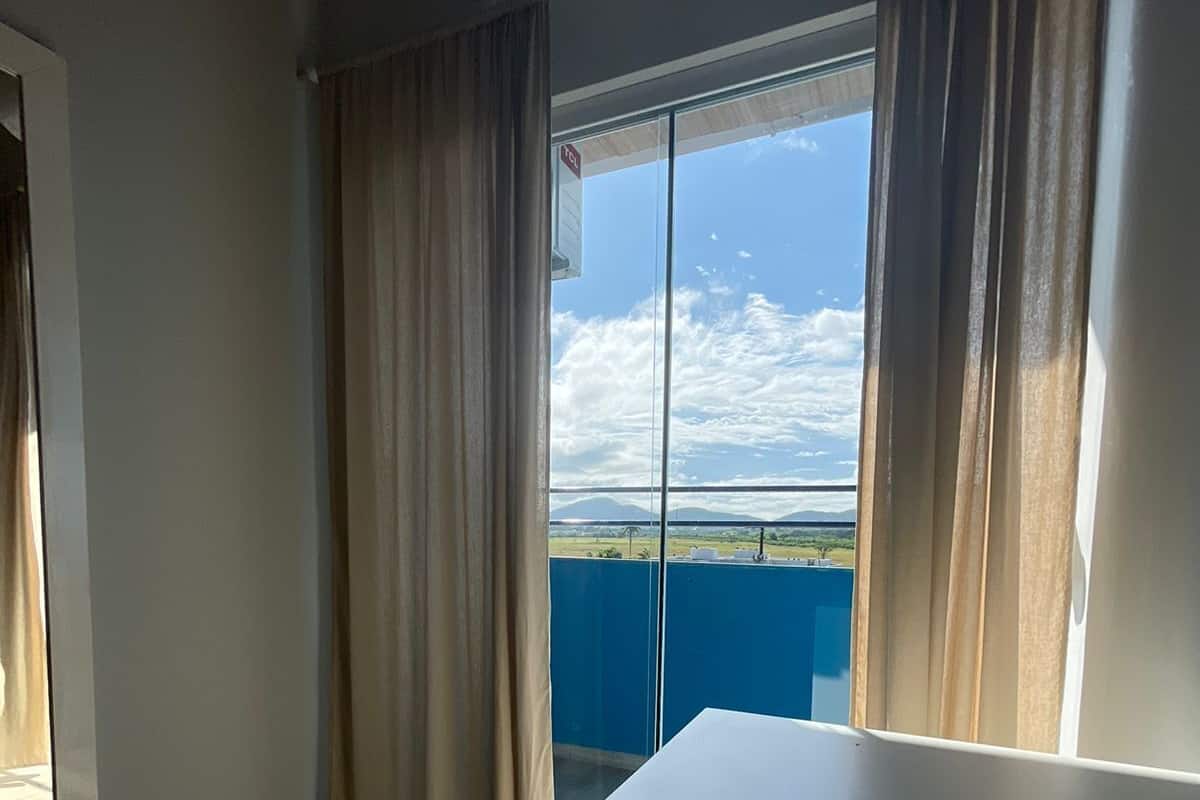 A room with a large window, a white table, and a ceiling-mounted air conditioner.