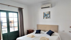 A hotel room with two beds, a window with curtains, an air conditioning unit, and a butterfly painting. - Villa Martina, Lugar Ideal Para Disfrutar Sol@ o en Familia (Playa Blanca)