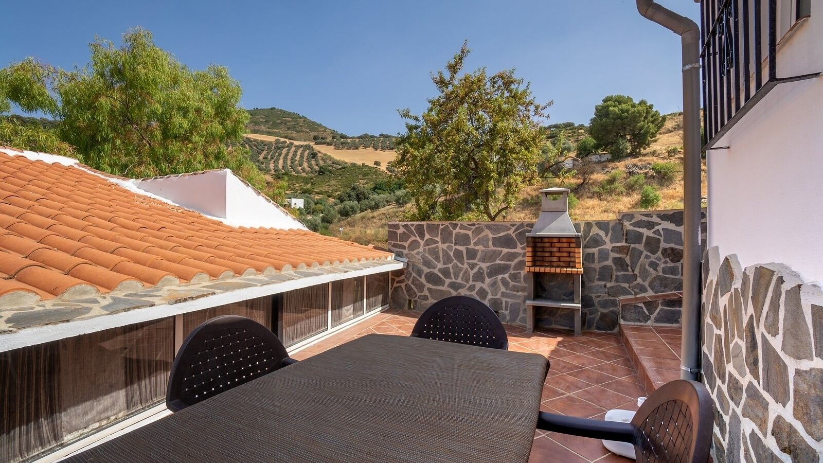 Un patio con mesa y sillas, un muro de piedra y una parrilla.