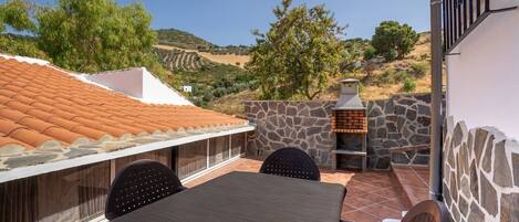 Un patio con mesa y sillas, un muro de piedra y una parrilla.