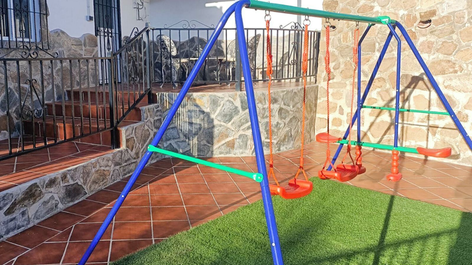 A children's play area with swings and a stone wall backdrop.