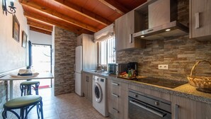 Een compacte keuken met een stenen spatwand, houten kastjes, een ingebouwde wasmachine en een koffiezetapparaat.