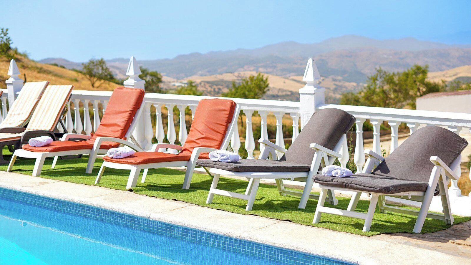 A poolside area with lounge chairs and a white fence.