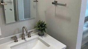 Ein Badezimmer mit einem weißen Waschbecken, einem Spiegel und einer Topfpflanze.