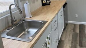Eine moderne Küche mit Spüle aus Edelstahl, einer Holz Arbeitsplatte und grauen Schränken.