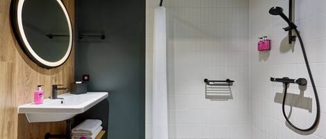A modern bathroom with a wooden vanity, a large mirror, a white sink, a shower area, and a towel rack.