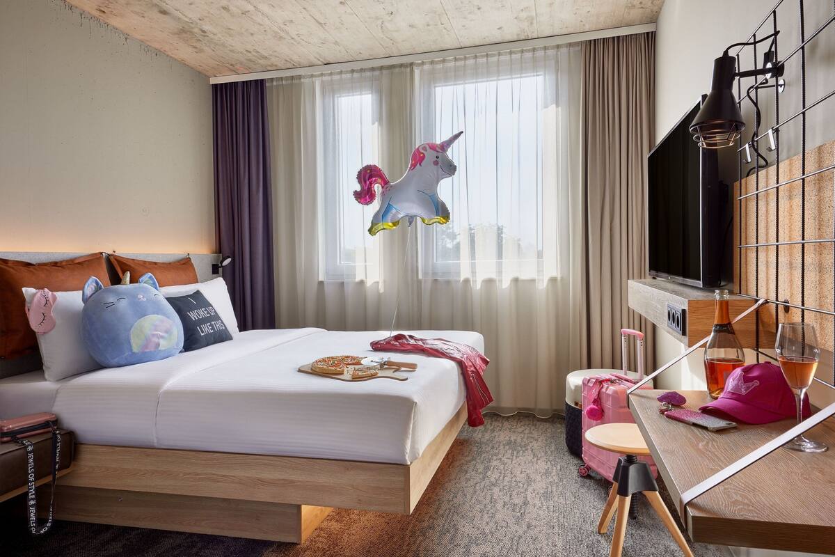 A hotel room with a bed, a desk, a TV, and a window with curtains.