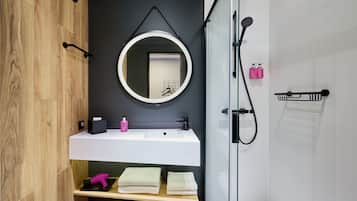 A modern bathroom with a wooden vanity, a round mirror, a white sink, and a glass shower enclosure.