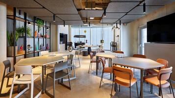 Un espace de bureau moderne doté de plusieurs tables et chaises, d’un grand écran de télévision, ainsi que d’étagères ornées de plantes et d’objets décoratifs.