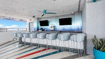 Eine moderne Bar mit einer langen Theke, mehreren Barhocker und zwei großen Bildschirmen an der Wand.