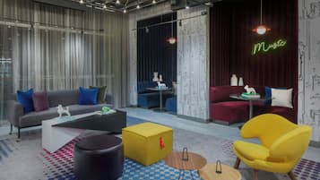 Un salon moderne avec un canapé gris, un pouf jaune et un fauteuil jaune. On aperçoit également une table basse noire, une petite table ronde et un canapé rouge à l’arrière-plan.