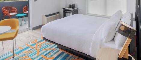 A hotel room with a large bed, a TV, a small table with chairs, and a view of the outside.