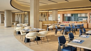 A modern dining area with tables and chairs, a kitchen in the background, and a curved ceiling design. - Fairfield By Marriott Jakarta Soekarno-Hatta Airport (Jakarta)