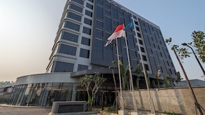 A modern hotel building with a curved glass facade, multiple floors, and a prominent sign. - Fairfield By Marriott Jakarta Soekarno-Hatta Airport (Jakarta)