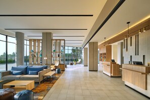 Eine großzügige Lobby mit Empfangstresen, einer Sitzecke und großen Fenstern mit Blick ins Freie.