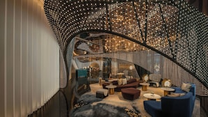 A modern interior with a curved ceiling adorned with lights, a seating area with sofas and tables, and a visible staircase. - W Macau - Studio City (Cotai)