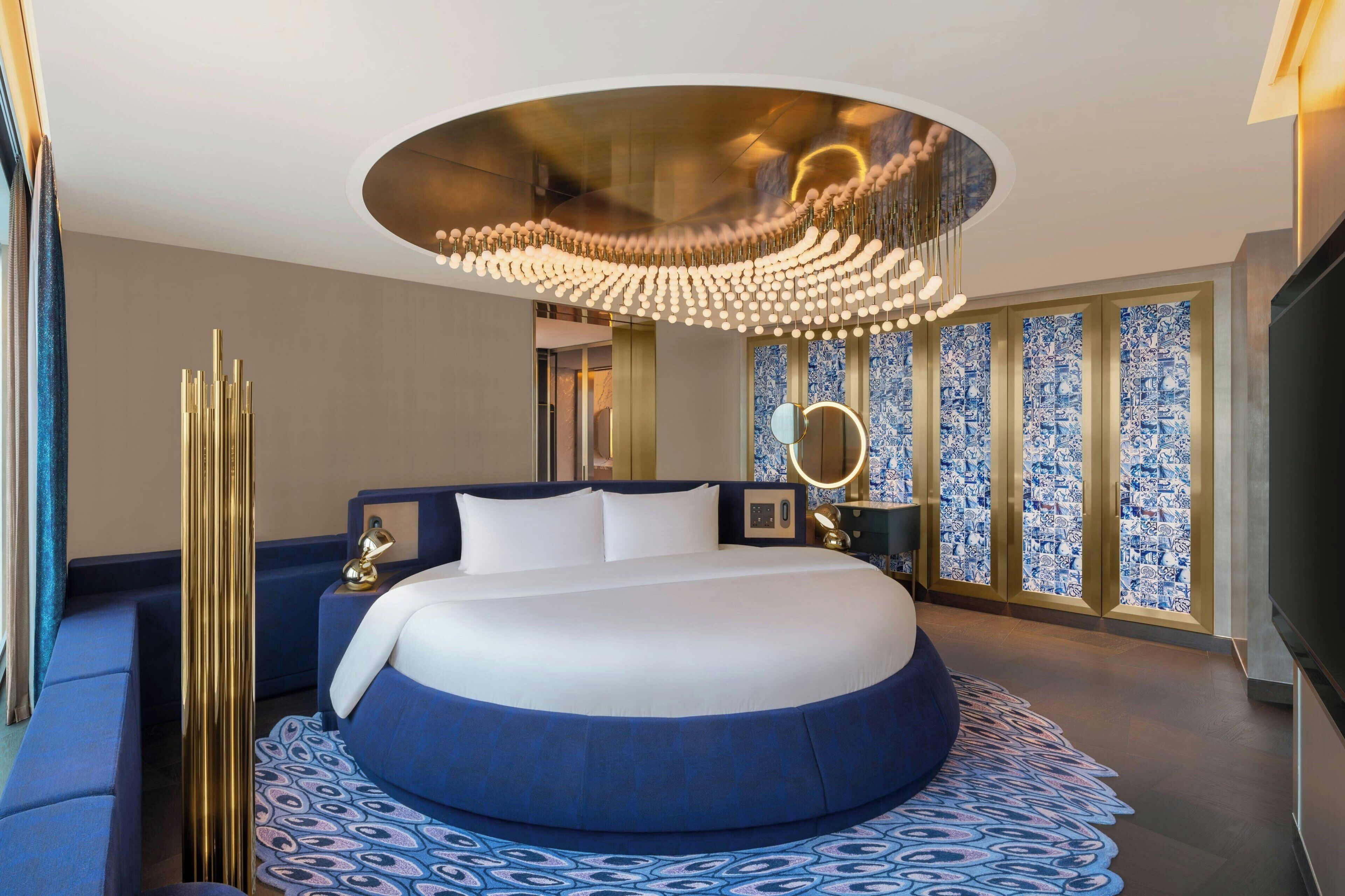 A modern hotel room with a round bed, a large mirror, and a unique ceiling design.