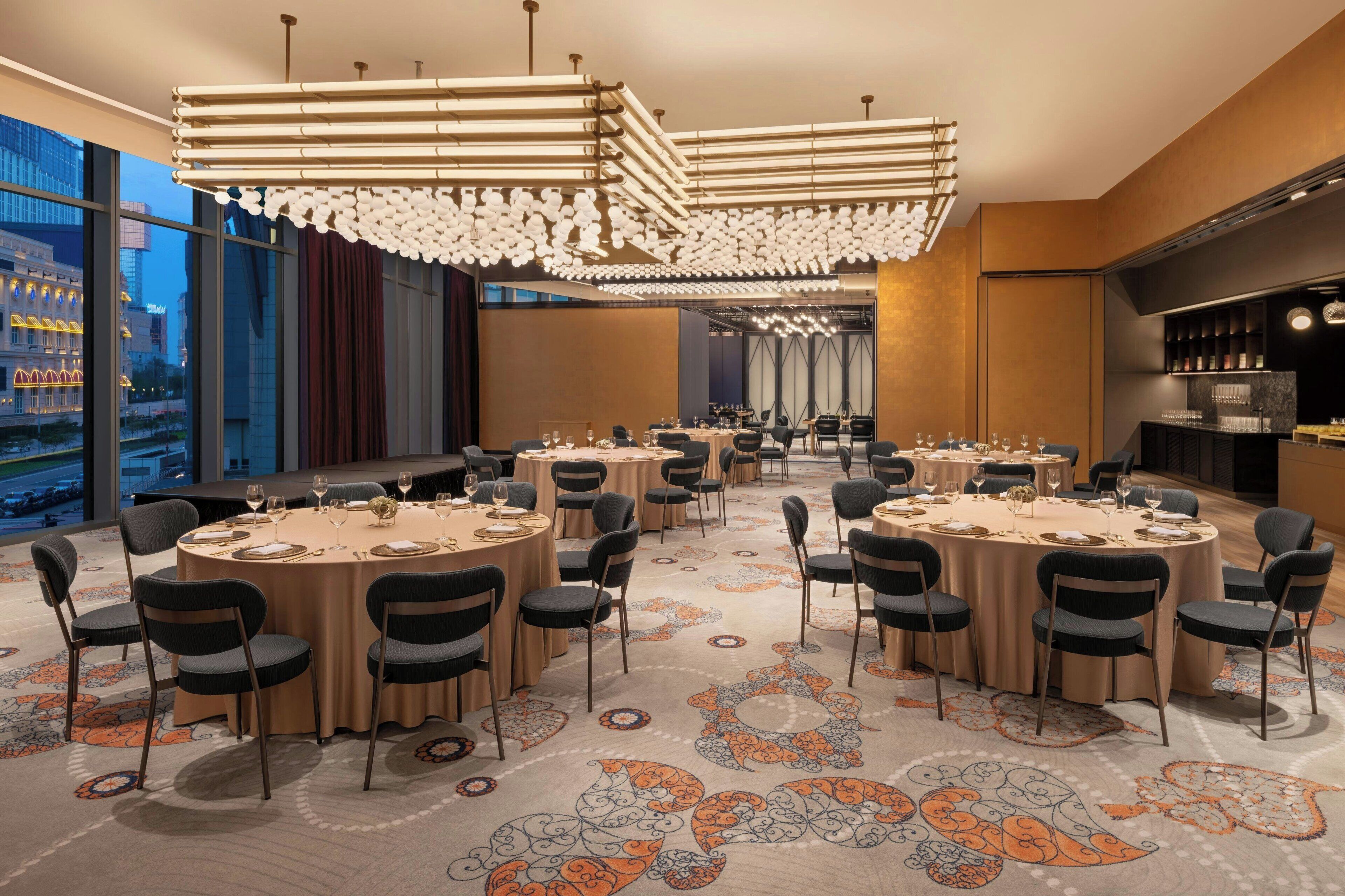 A modern hotel dining area with round tables, black chairs, and a patterned carpet.