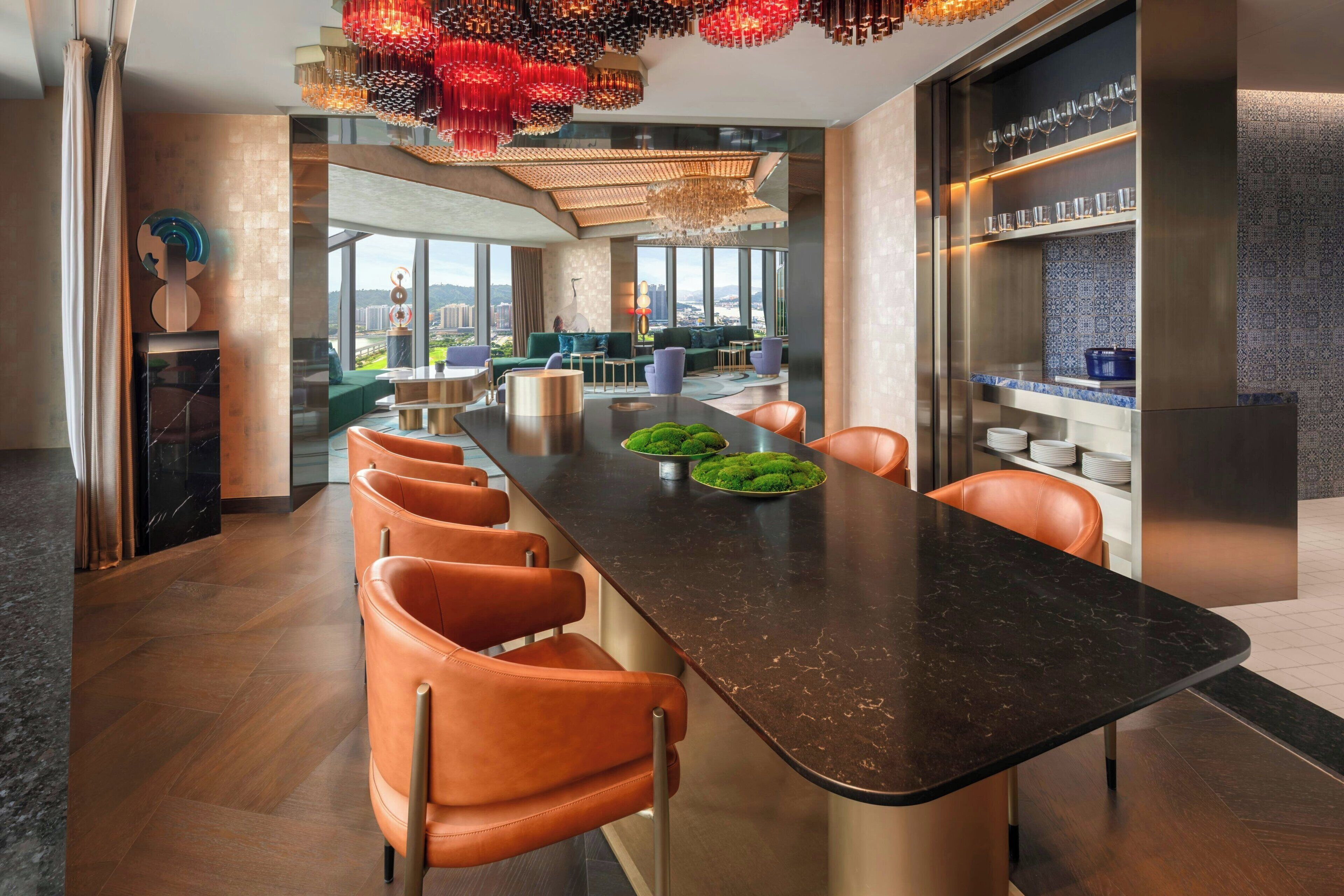 A modern kitchen with a long island, orange chairs, and a view of the city.