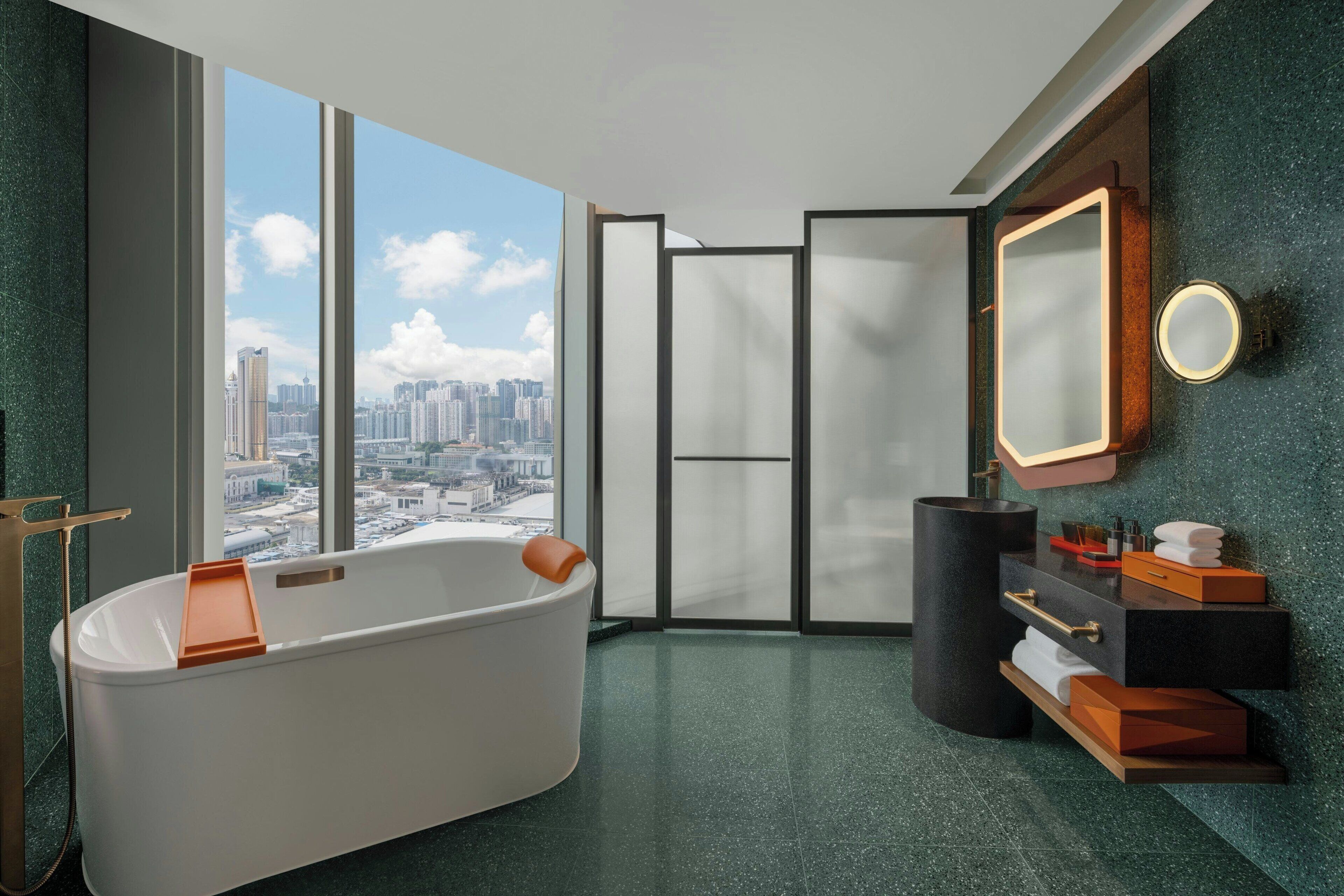 Un baño moderno con una bañera independiente, un espejo grande y vistas de la ciudad a través de amplias ventanas.