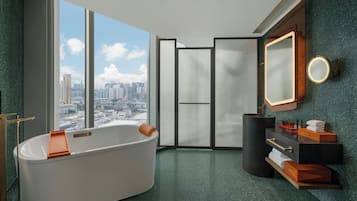 Un baño moderno con una bañera independiente, un espejo grande y vistas de la ciudad a través de amplias ventanas.