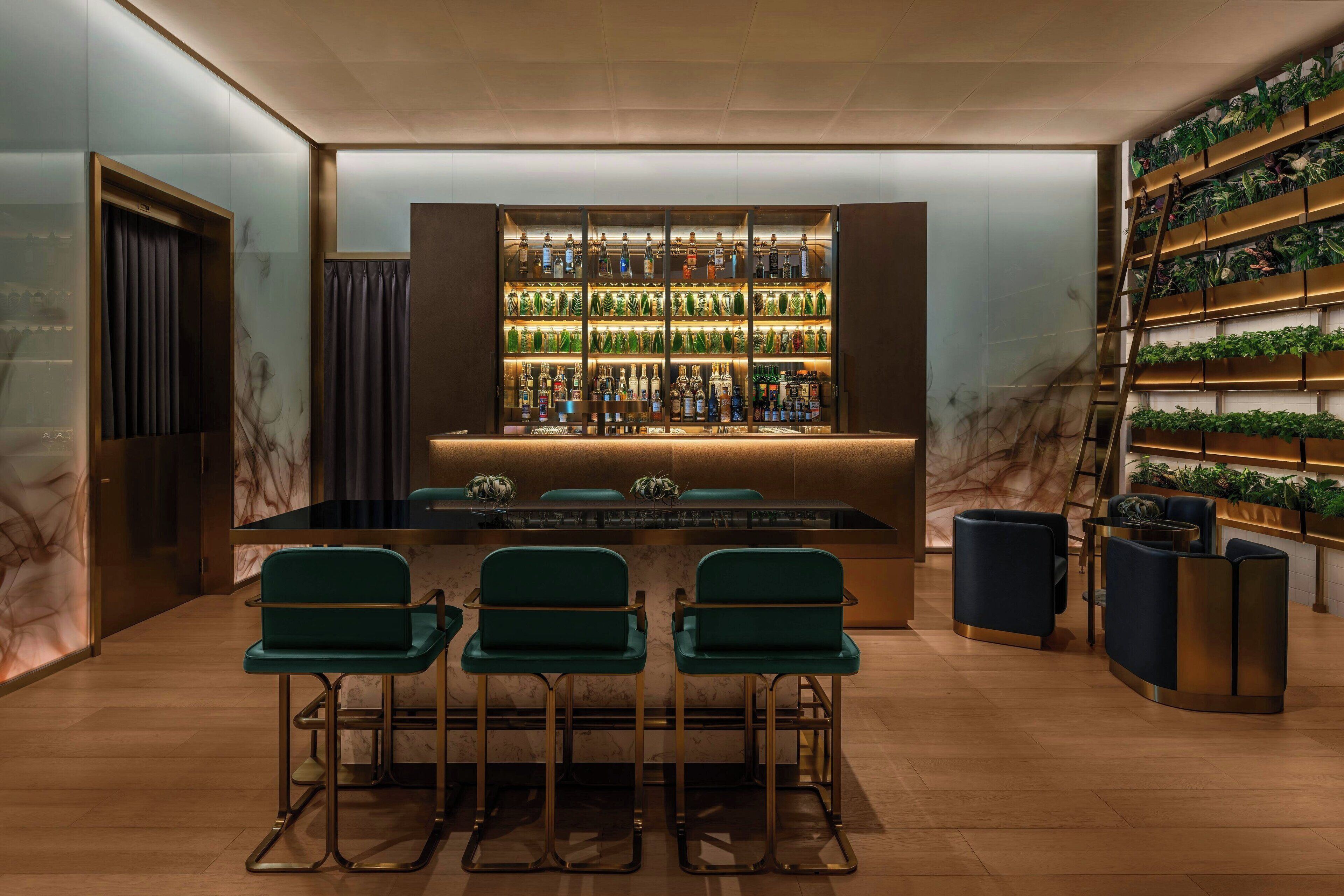 A bar area with a marble wall, green bar stools, and shelves of bottles.