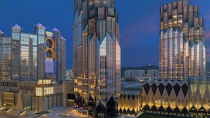 A modern high-rise building with a unique geometric facade, surrounded by other contemporary structures. - W Macau - Studio City (Cotai)