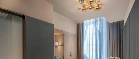 Una habitación de hotel moderna con cama, zona de estar, tocador y un ventanal con cortinas.