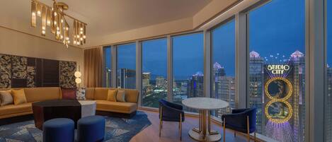 A modern living room with a city view, a sofa, ottomans, a coffee table, and a chandelier.