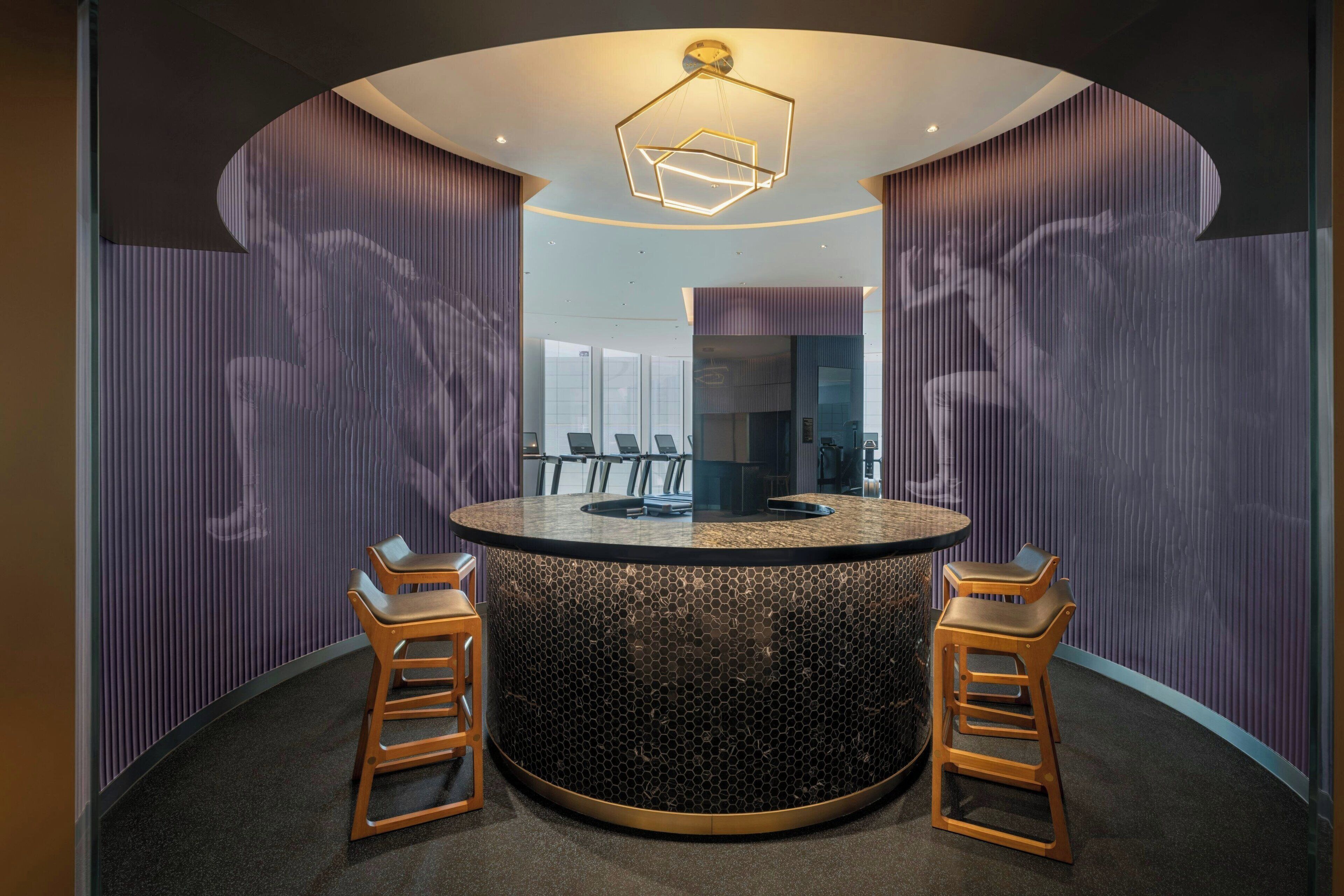 A modern reception area with a circular counter, two wooden bar stools, and a unique geometric light fixture.