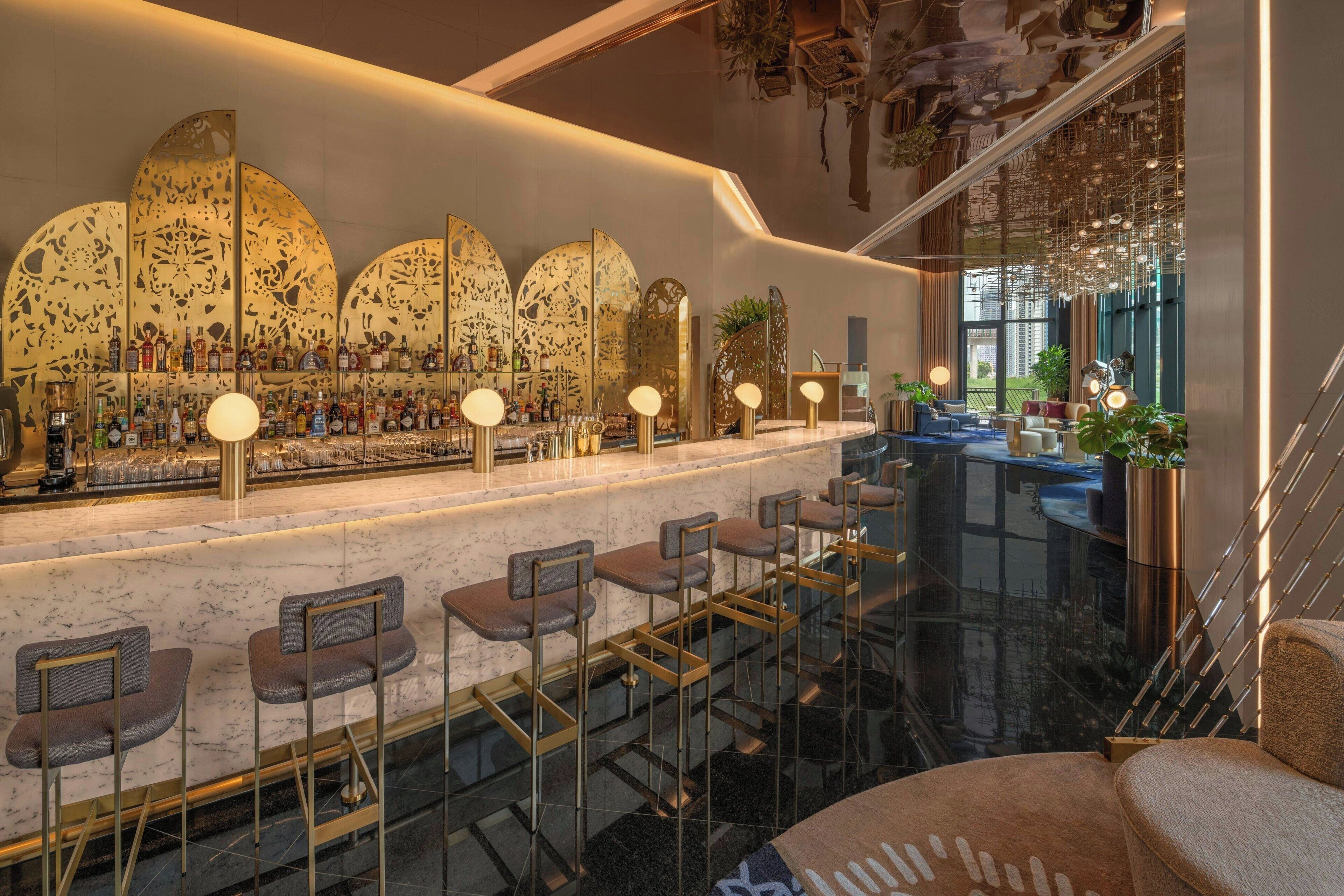 A bar area with a marble countertop, multiple bar stools, and a variety of bottles.