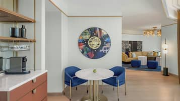 A modern kitchen with a round table and chairs, a coffee machine, and a decorative wall piece.