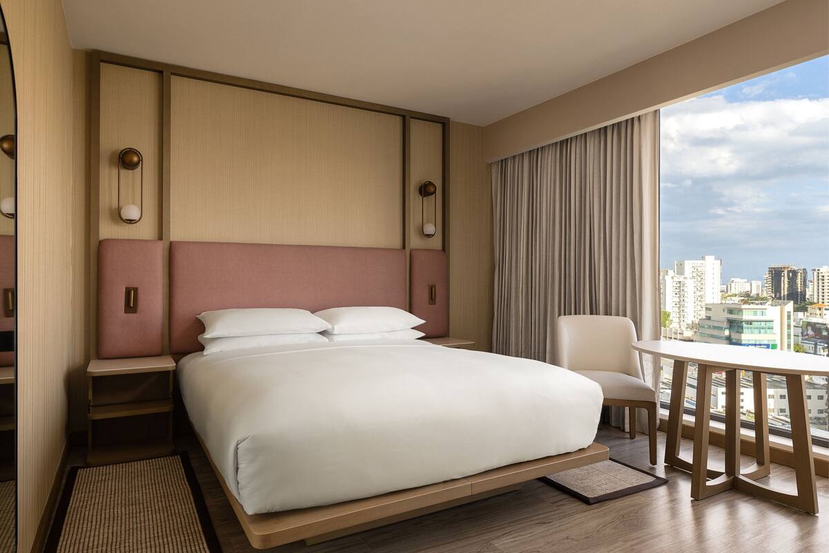 A modern hotel room with a large bed, a desk, and a view of the city.