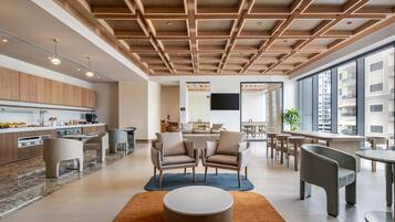 Un vestíbul d'hotel modern amb una zona de cuina, zones d'estar i grans finestres que ofereixen vistes a la ciutat.