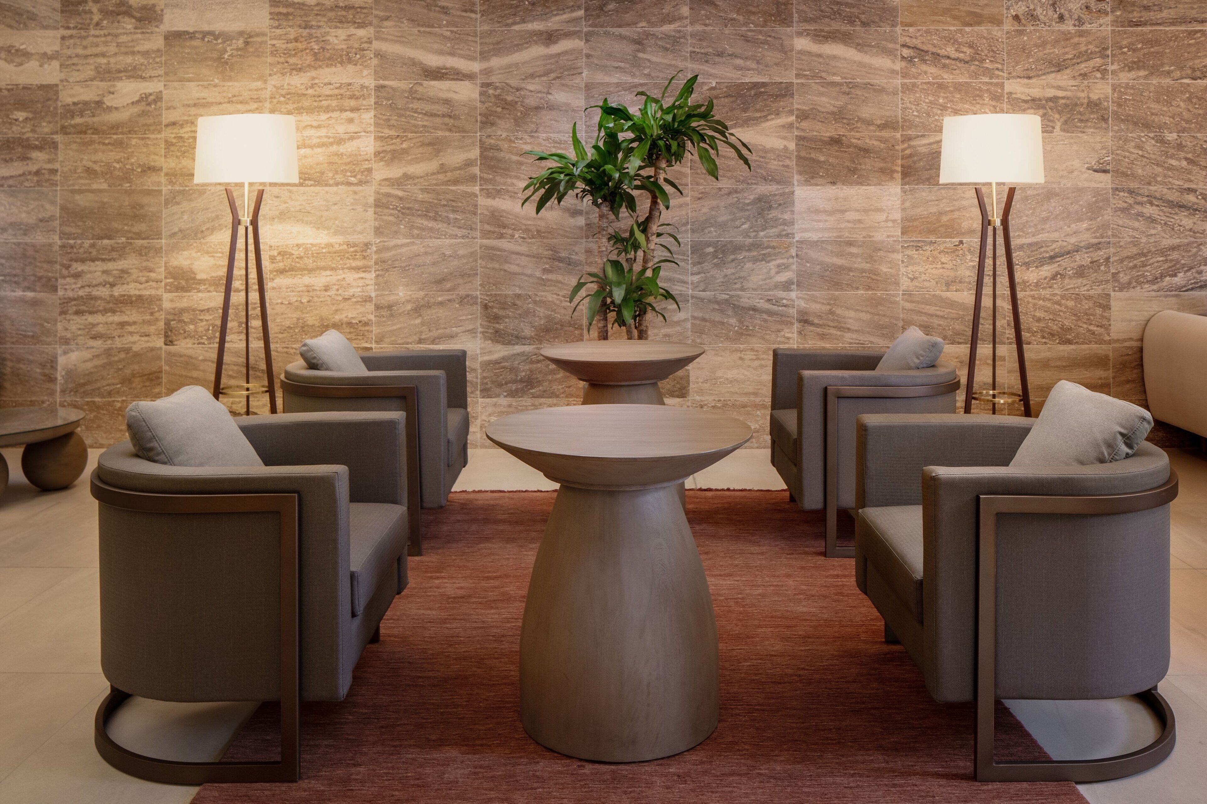 Un hall d’entrée moderne avec une table ronde centrale, quatre fauteuils gris, deux lampadaires et une plante en pot.