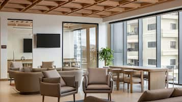 A modern living room with a wooden ceiling, large windows, and a flat-screen TV mounted on the wall.