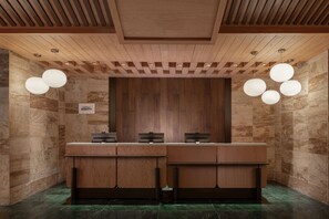 Zona de recepción con un mostrador de madera, paredes de mármol e iluminación colgante.
