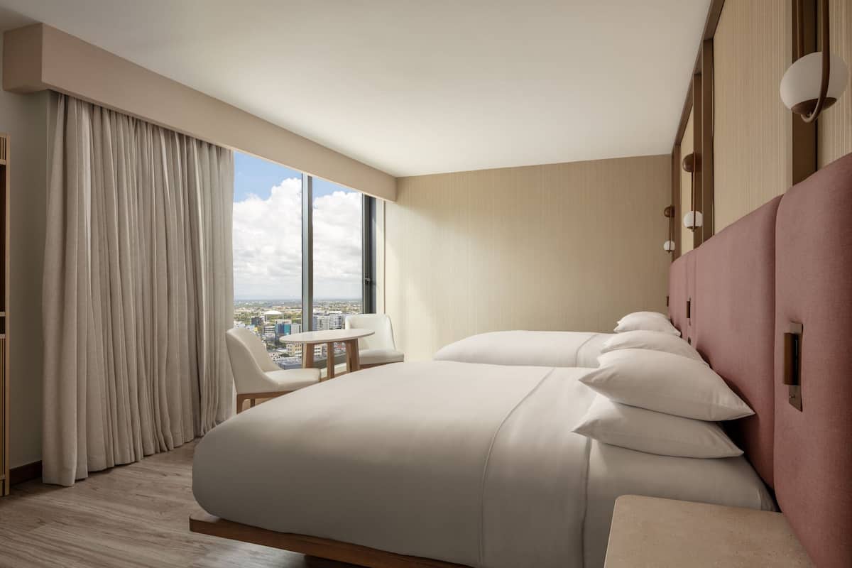 A modern hotel room with a large bed, a small table, and a view of the city.