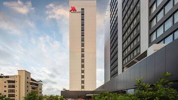 A tall hotel with a prominent 'Marriott' sign, surrounded by greenery and other buildings.