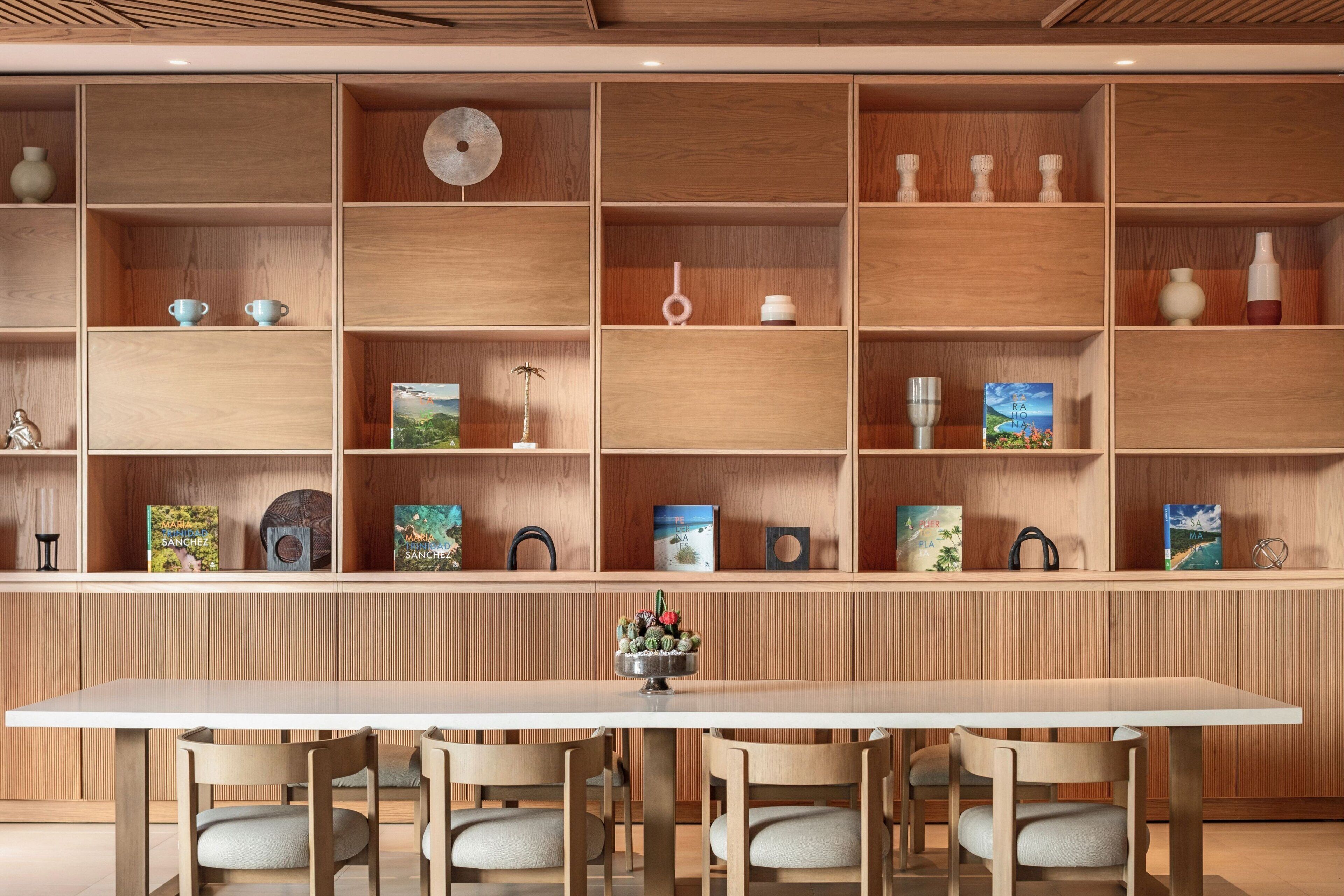 Un intérieur moderne avec une longue table en bois et des chaises assorties, entouré d’étagères en bois où sont disposés divers objets décoratifs et des livres.