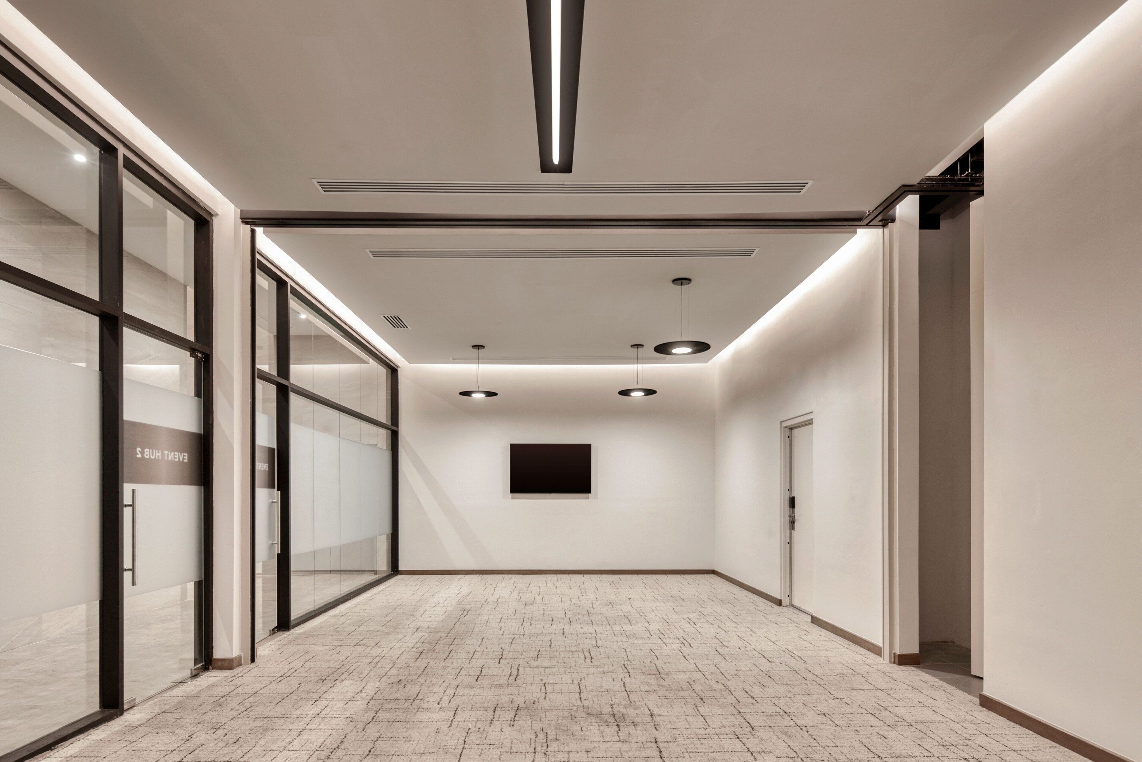 A modern hallway with a tiled floor, glass doors, recessed lighting, and a flat-screen TV mounted on the wall.