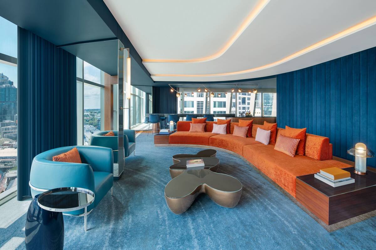 A modern living room with a large orange sofa, blue armchairs, and a unique coffee table.